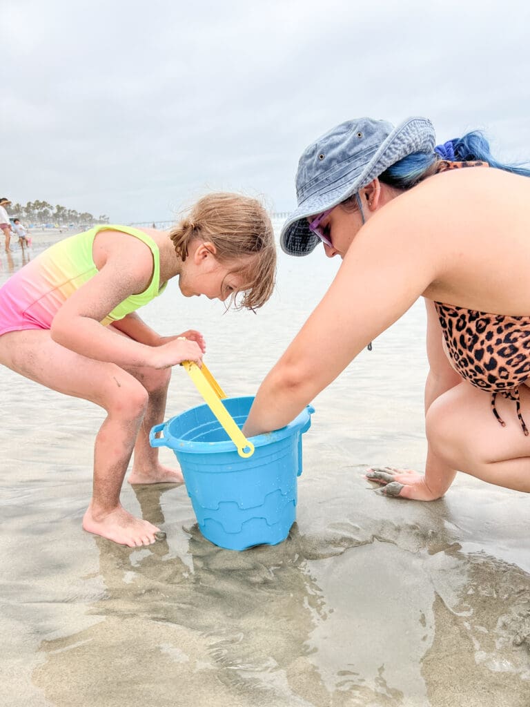 two girls at the beach looking into a blue sand bucket.