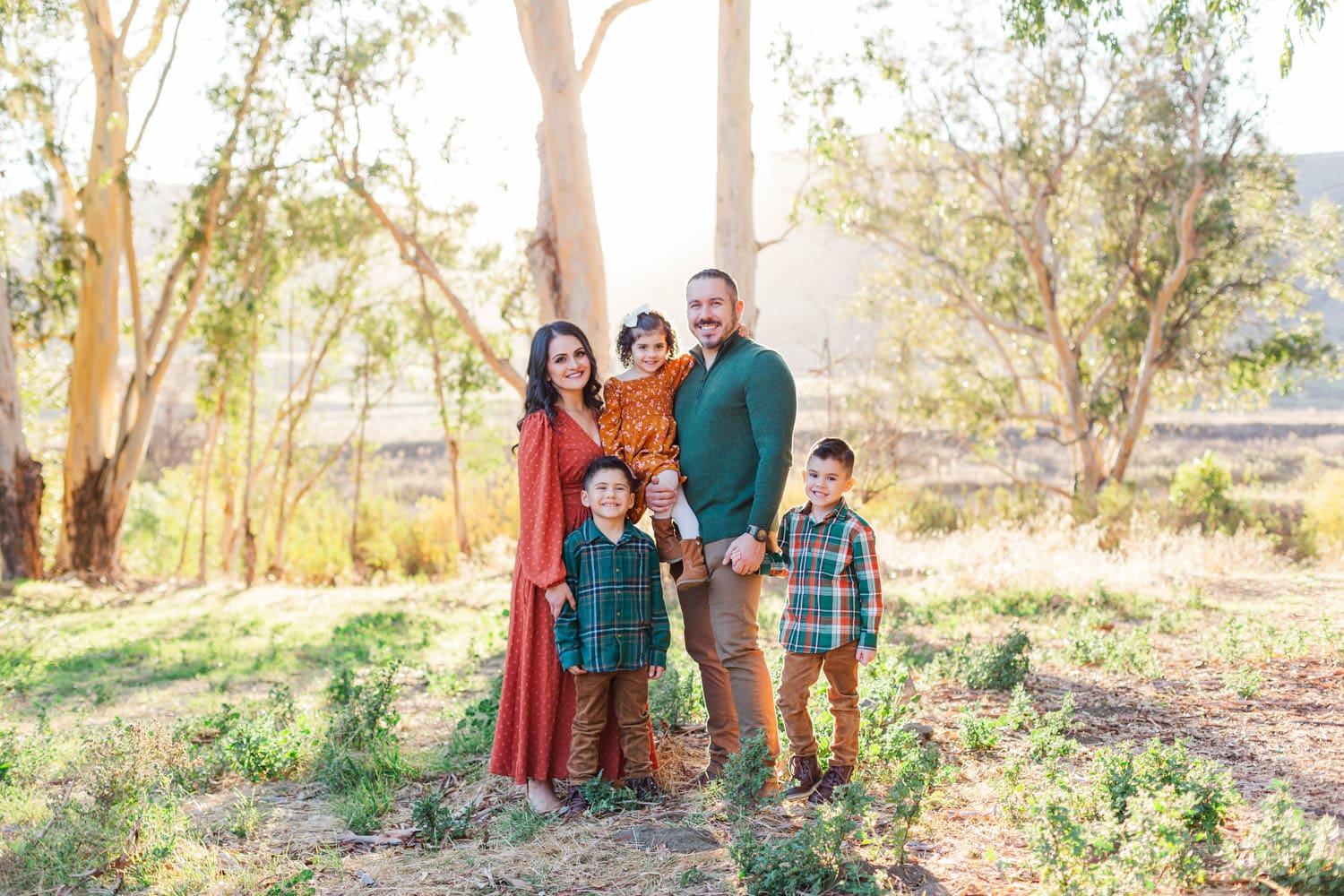 family of five standing together with trees and bushes in the background