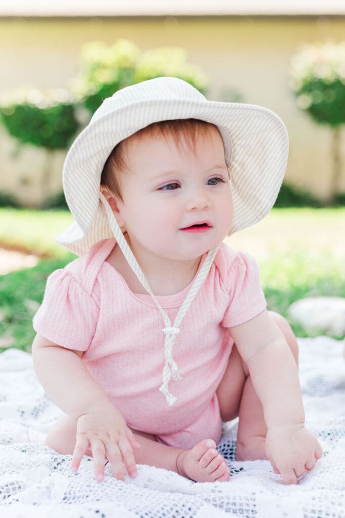 Baby girl wearing a cream bucket hat and pink romper and smiling