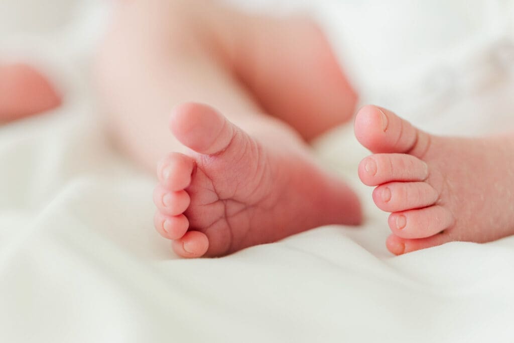 Close up of a newborns feet and toes while laying on a white blanket.