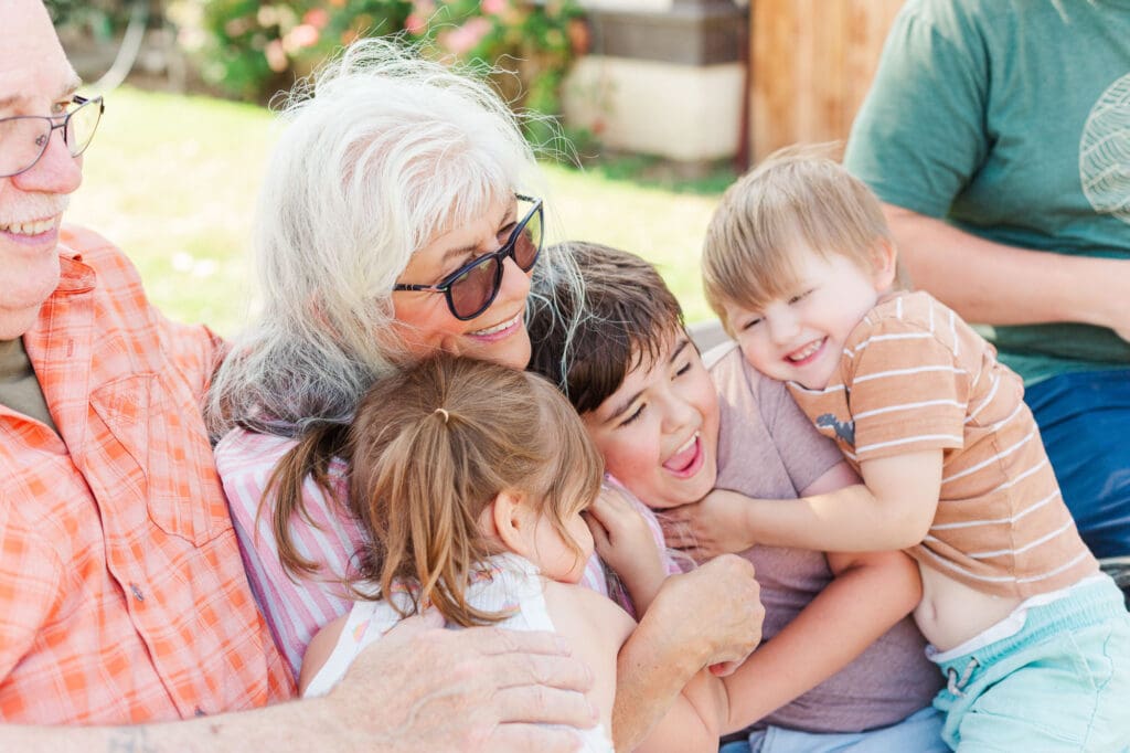 an older lady wearing glasses is hugging three children.