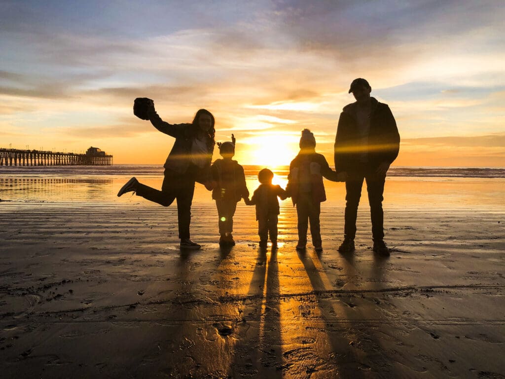a silhouette of 5 people standing on the beach with the sunsetting behind them.