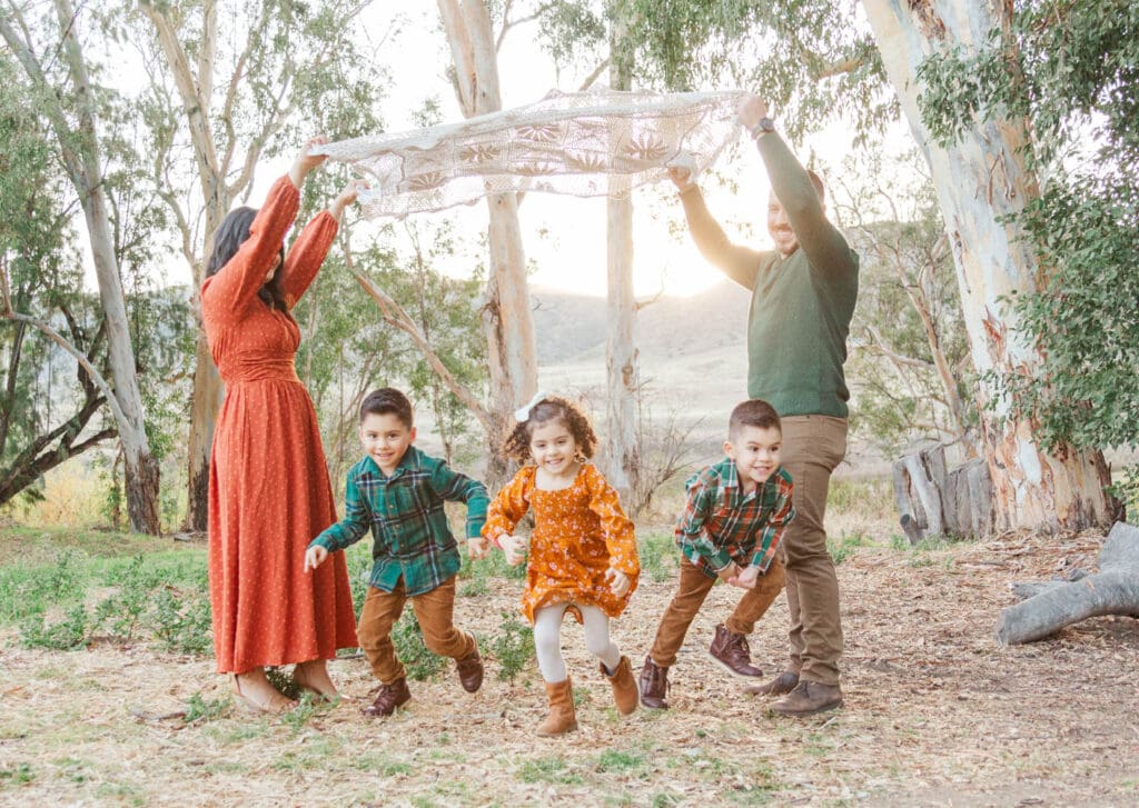 mom and dad holding a blanket up in the air while their kids run under it.