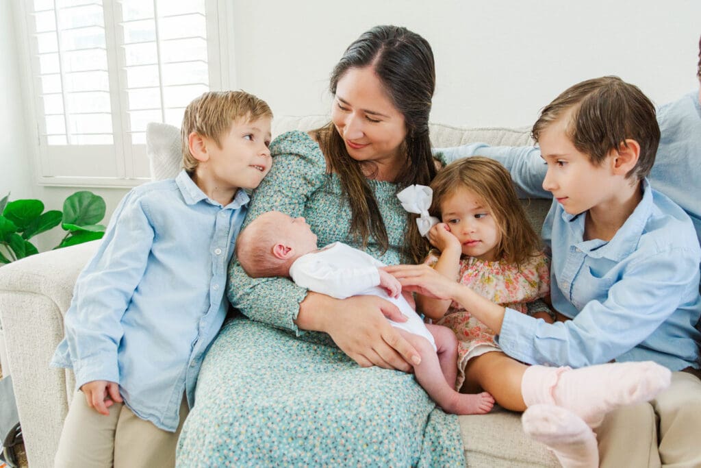 Mother and son looking at each other while holding her newborn sitting on a couch with her family around her and baby.
