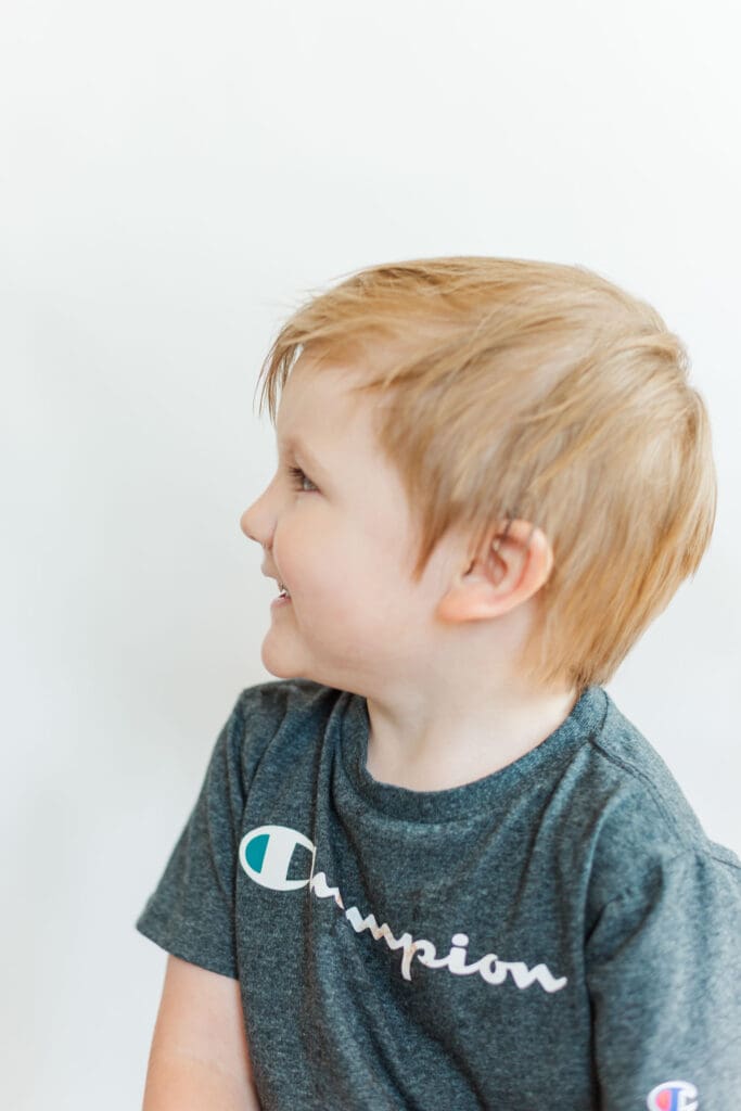 Profile of a little boy wearing a grey shirt in front of a white background smiling off to the side.