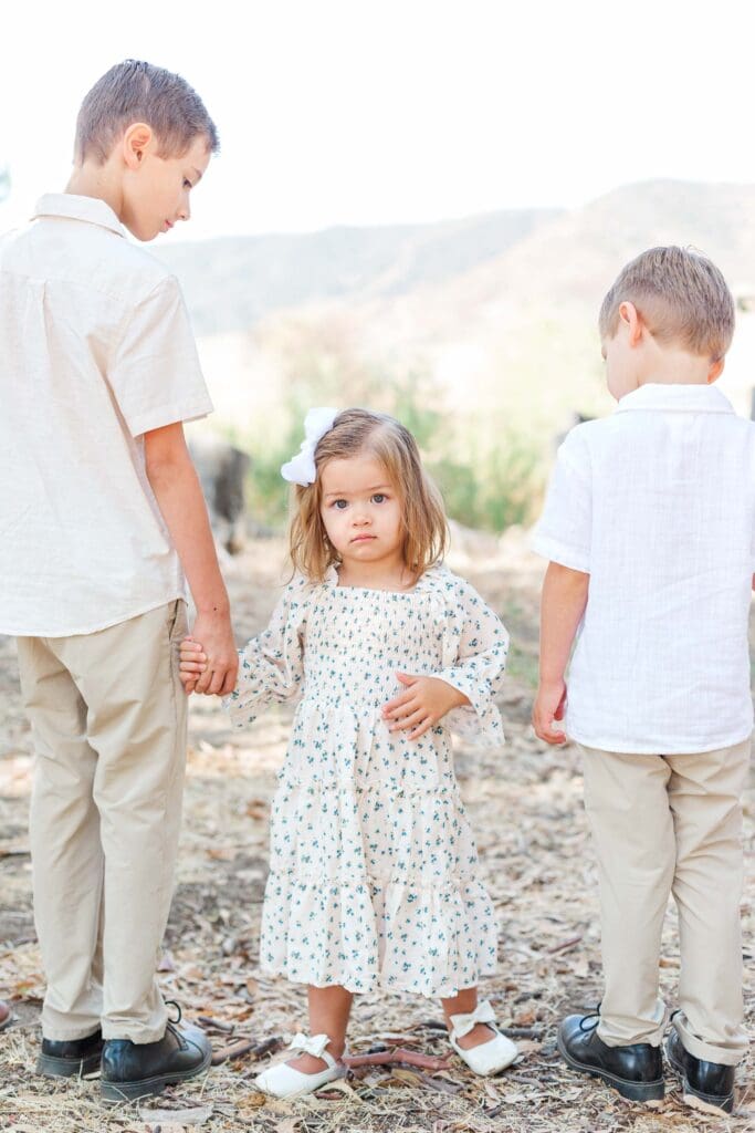 two boys are facing away from the camera holding a girls hand while the little girl is looking at the camera.
