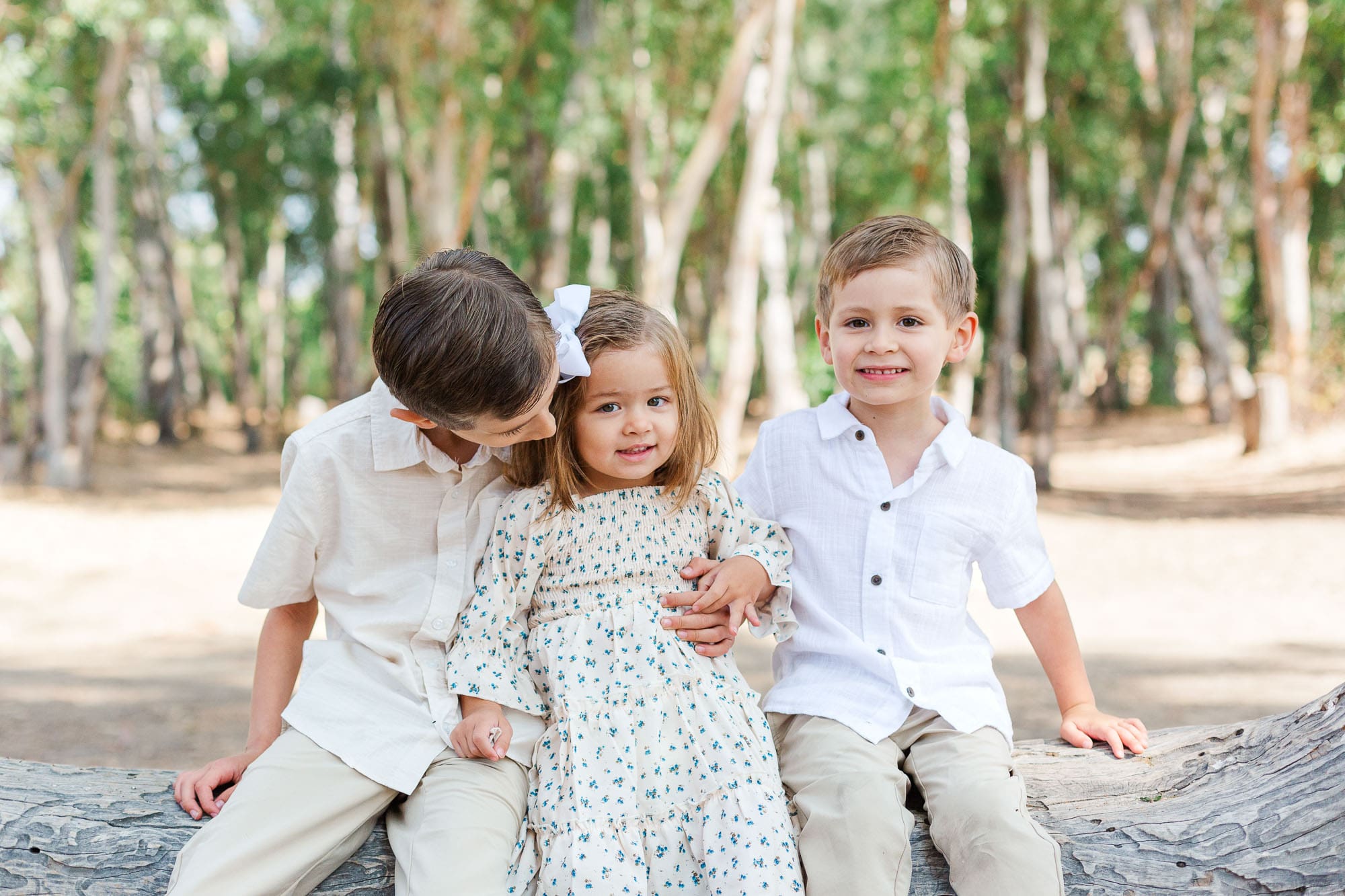 three smiling children sitting on a log.