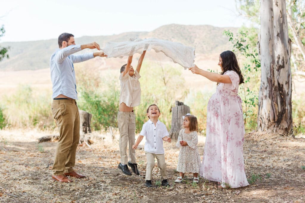 mom and dad are holding a blanket while the kids stand under it and jumping up to touch the blanket.