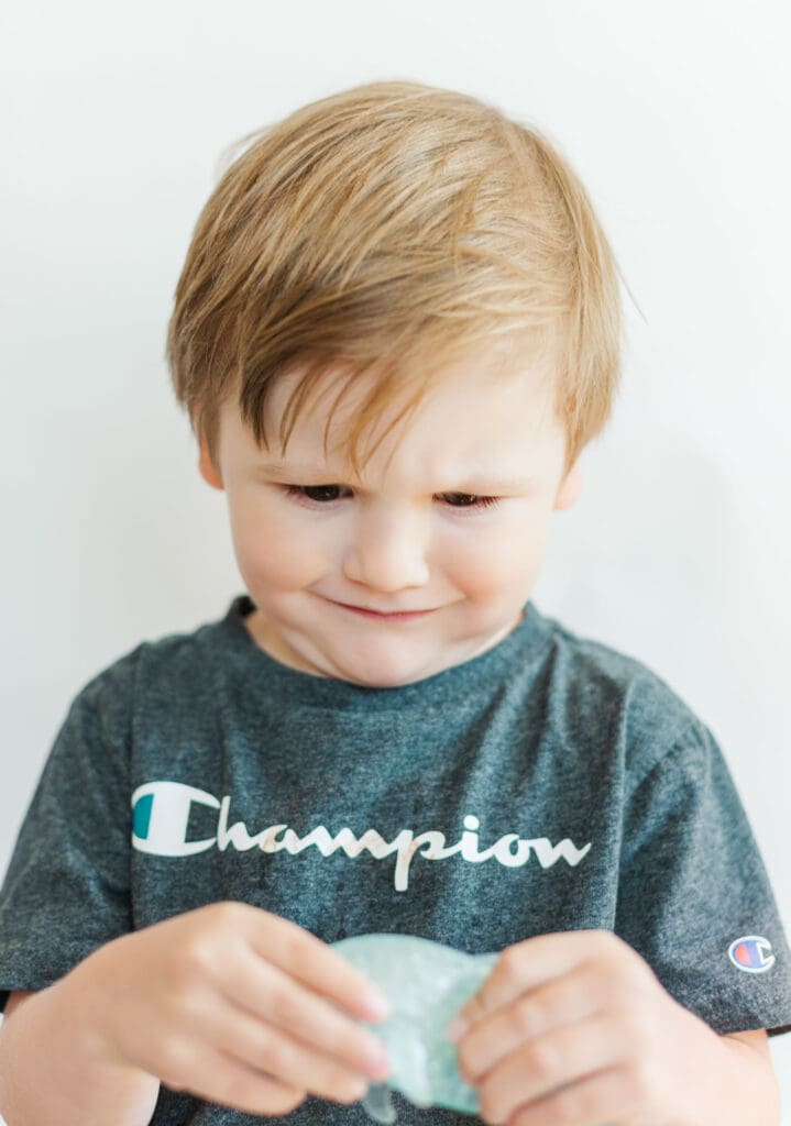 Little boy wearing a grey shirt in front of a white background making a frowning face.