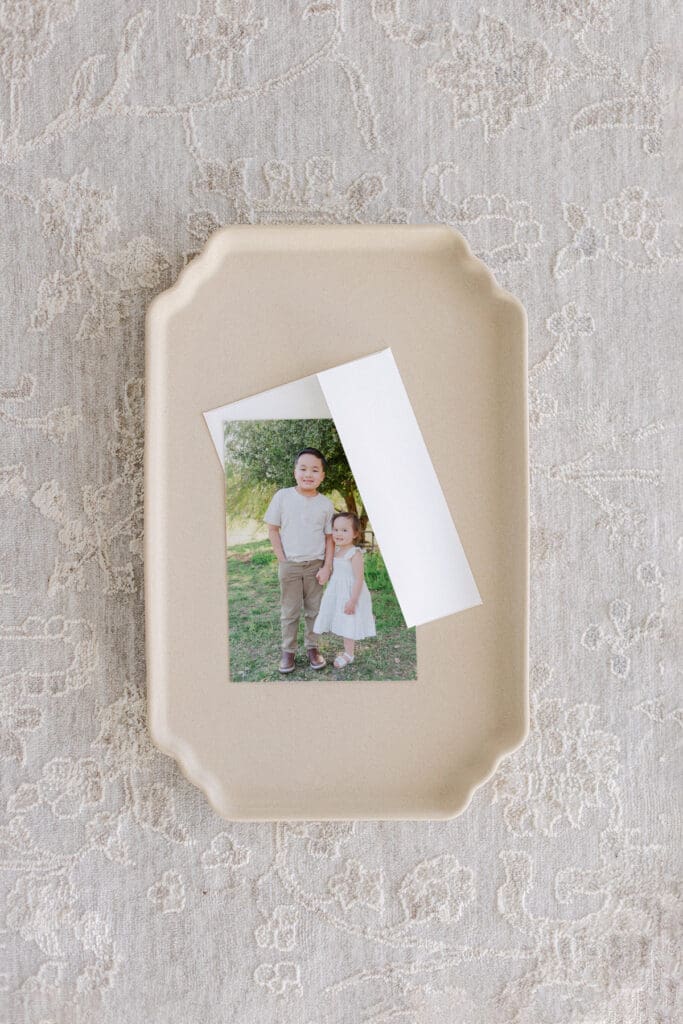 a photo card of a brother holding his sister's hand and the card is resting on a cream plate.