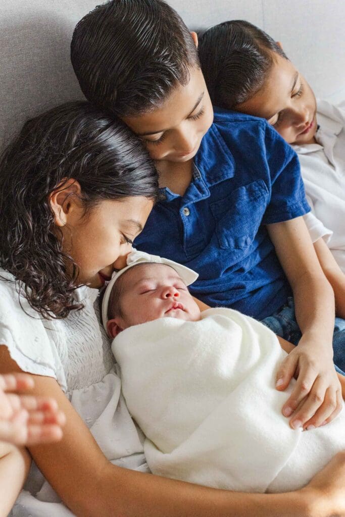 siblings holding their newborn sister and older sister is snuggling with baby