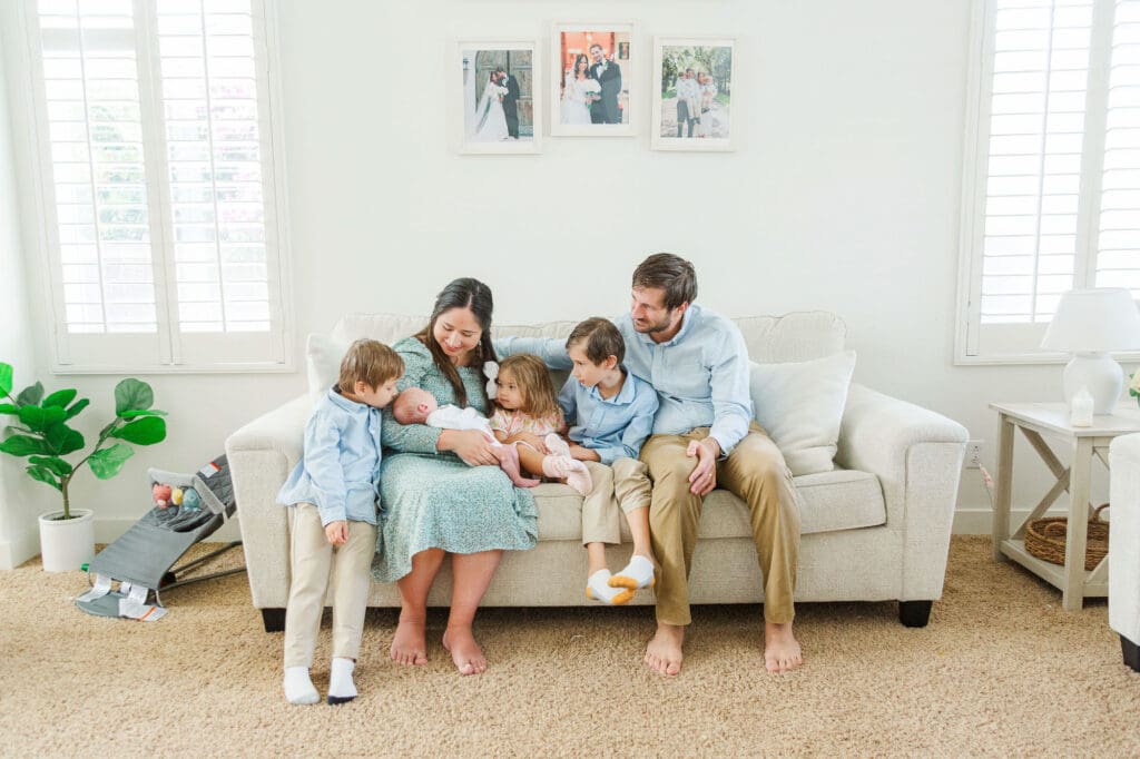 family sitting on a white couch with their whole family while they all look at newborn