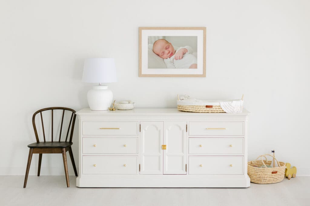 portrait of a baby in a white matted frame above a white dresser