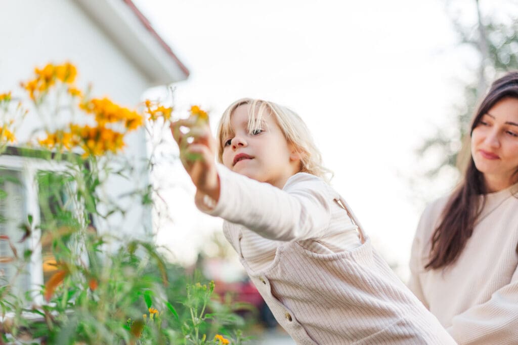 A young girl picking wildflowers in a sun-filled Temecula field during a lifestyle family photography session.